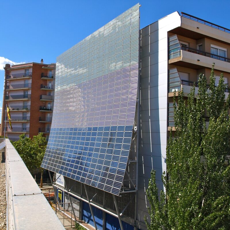 Gran instalacion fotovoltaica montada en la fachada de un edificio, con bloques de viviendas a ambos lados