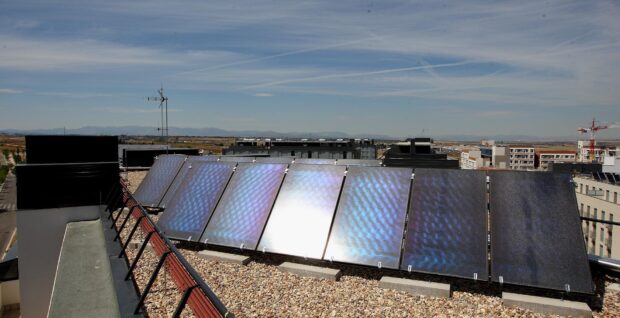 Fila de captadores solares sobre la cubierta plana de un edificio de viviendas, con mas bloques y una grua al fondo